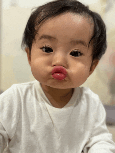 a baby wearing a white shirt is making a funny face with his mouth open