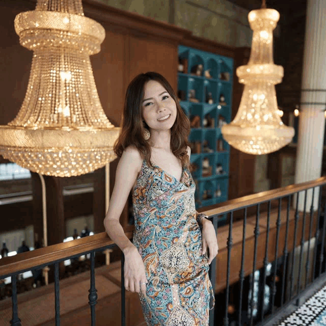 a woman in a dress stands on a railing in front of chandeliers