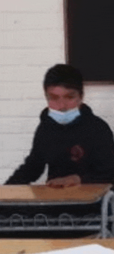 a boy wearing a mask sits at a desk in a classroom .