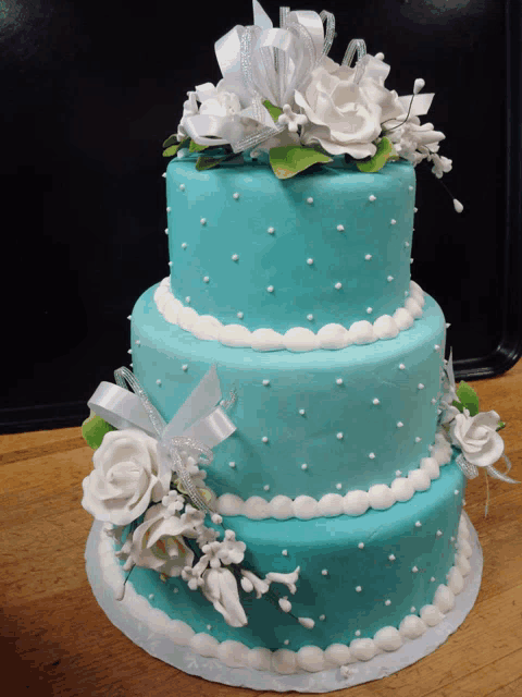 a blue cake with white flowers and pearls on top