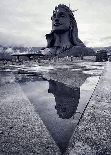 a black and white photo of a statue of lord shiva with his reflection in the water .