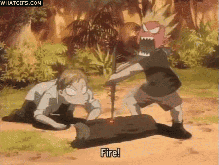 a man is laying on the ground while another man throws a stick at a fire .