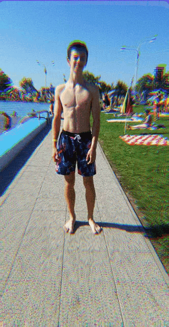 a shirtless young man in swim trunks stands on a sidewalk