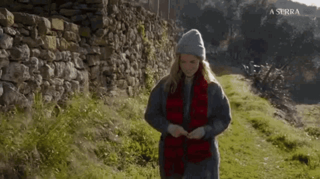 a woman wearing a scarf and a hat is walking in a field with a a serra logo behind her