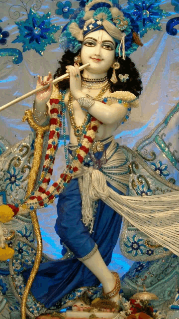 a statue of krishna playing a flute in a blue and white dress