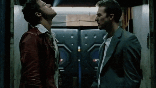 a man in a suit and a man in a red jacket are looking up at each other