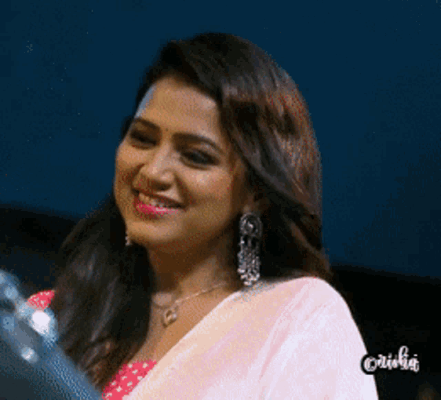 a woman wearing a pink saree and earrings smiles for the camera with the word caribbean on the bottom right