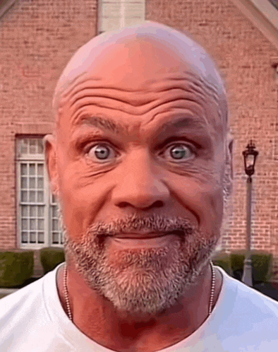 a bald man with a beard is making a funny face in front of a brick house .