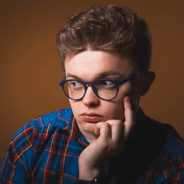 a young man wearing glasses and a plaid shirt is thinking