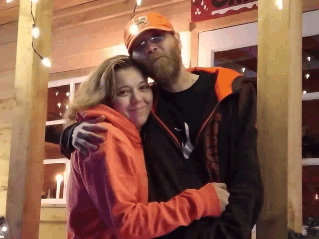 a man wearing an orange hat with the word eagles on it hugs a woman