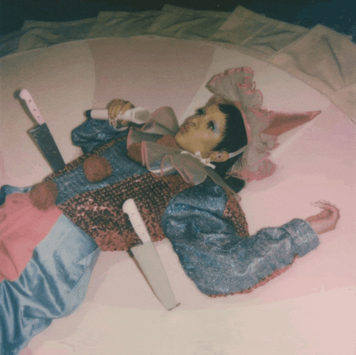 a woman in a clown costume is laying on the floor holding a microphone and two knives