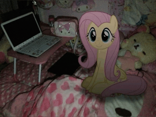 a picture of a pony sitting on a bed next to a laptop