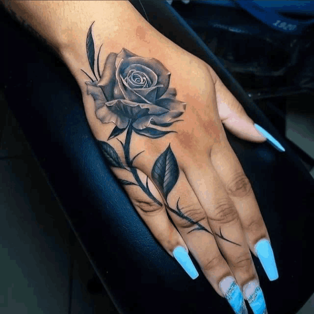 a woman with long blue nails has a black rose tattoo on her hand