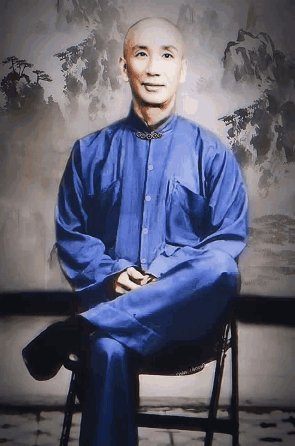 a bald man in a blue shirt sits on a chair