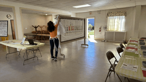 a woman in an apron holds up a sign that says " i love you " in a room with tables and chairs