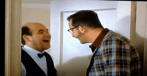 two men are laughing while standing next to each other in a room .