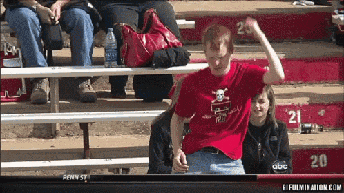 a man in a red shirt with a skull and crossbones on it stands in front of a bleacher with the number 20 on it