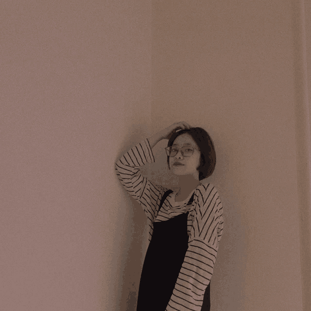 a woman wearing glasses and a striped shirt is standing in a corner