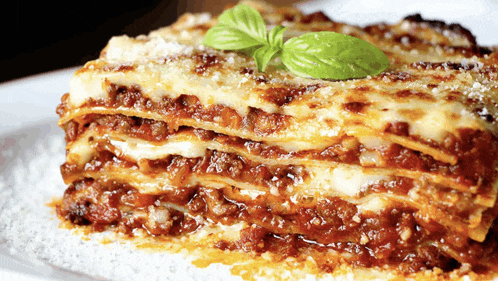 a white plate topped with a slice of lasagna with basil on top