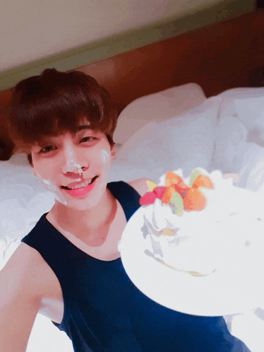 a young man with frosting on his face holds a plate of cake