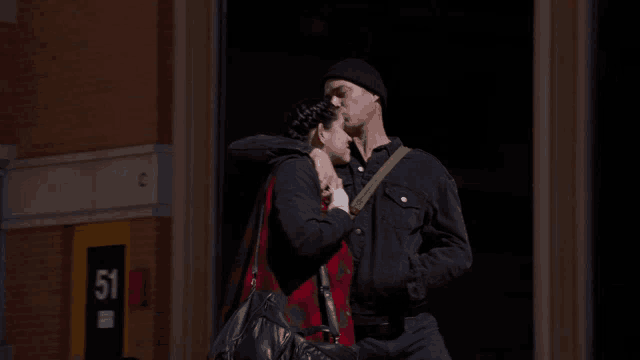 a man and woman kiss in front of a building with the number 51