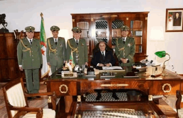 a group of men in military uniforms are standing around a man 's desk