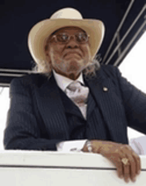 a man wearing a suit and a cowboy hat is leaning on a railing