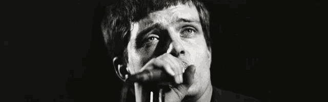 a black and white photo of a man singing into a microphone in a dark room .