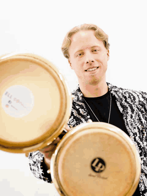 a man in a sequined jacket holds two lp drums in his hands