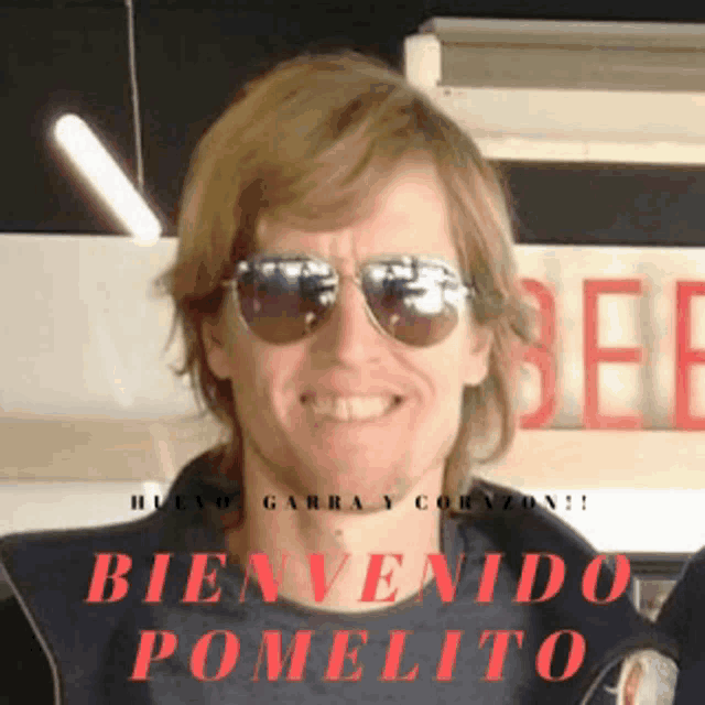 a man wearing sunglasses stands in front of a bienvenido pomerito sign