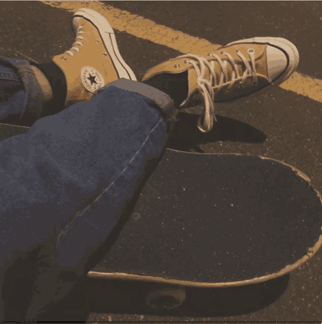 a person wearing a pair of yellow converse shoes is laying on a skateboard