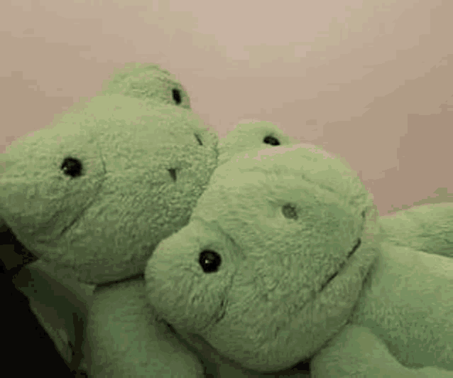 two green stuffed animals are sitting next to each other on a bed .