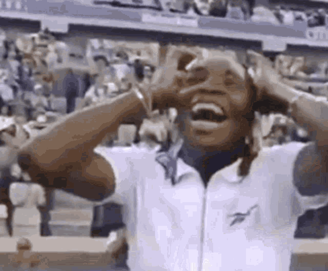 a man is laughing with his hands on his head in front of a crowd at a tennis match .