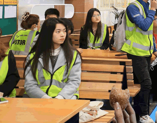 a girl wearing a yellow vest with the word visitor on it sits in a classroom