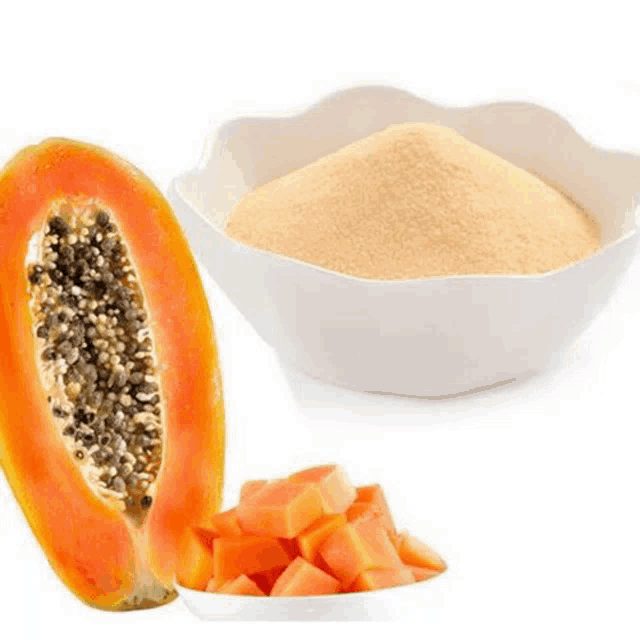 a papaya cut in half next to a bowl of papaya powder and sliced papaya .