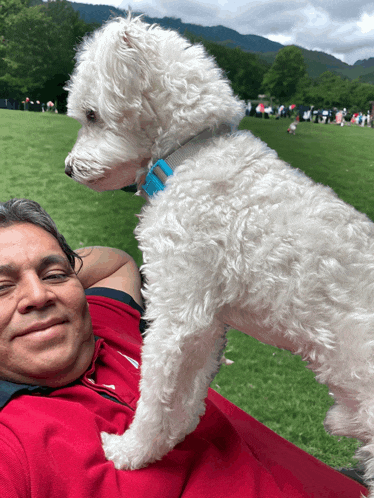 a man in a red shirt is holding a white dog