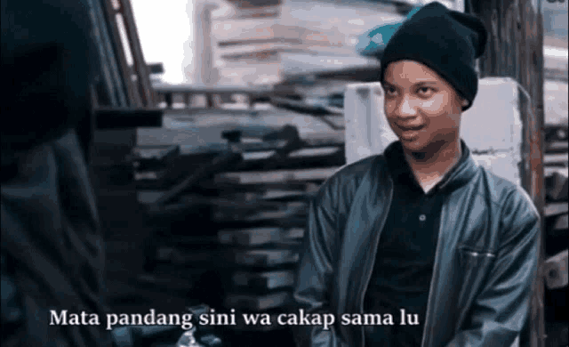 a man wearing a black beanie and a black jacket with the words mata pandang sini wa cakap sama lu on the bottom