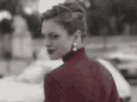 a woman wearing a red turtleneck sweater and earrings is standing in front of a car .