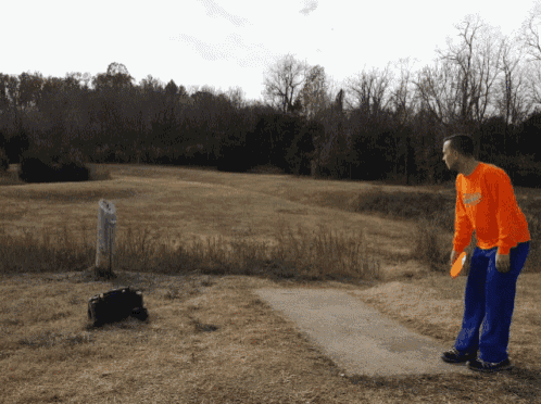 a man throwing a frisbee in a field while wearing an orange shirt that says ' georgia ' on it