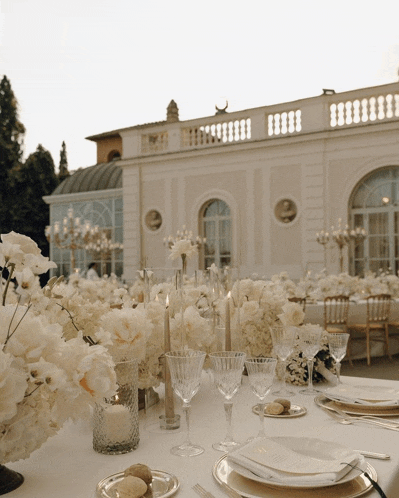 a table set with plates glasses and candles in front of a white building