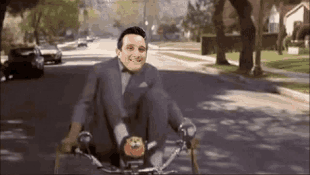 a man in a suit and bow tie is riding a bike down a street .