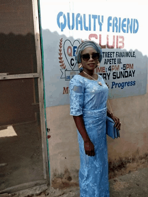 a woman in a blue dress is standing in front of a quality friend club sign