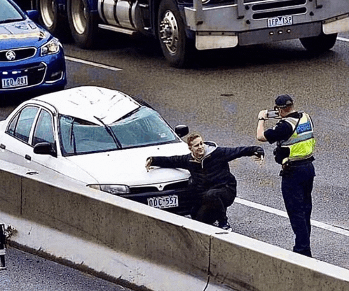 a police officer is taking a picture of a man sitting next to a car