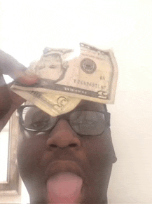 a man wearing glasses is sticking his tongue out and holding a 5 dollar bill on his head .