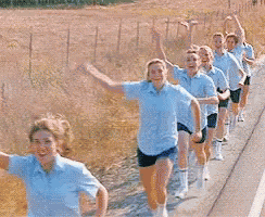 a group of women in blue shirts and shorts are running down a road with their arms in the air