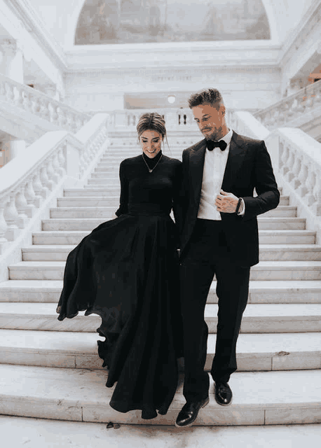 a woman in a black dress and a man in a tuxedo are walking down stairs