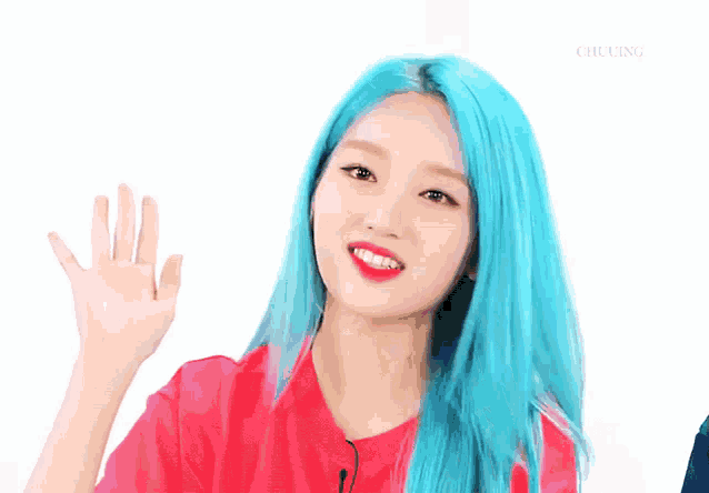 a girl with bright blue hair is wearing a red shirt and waving her hand .