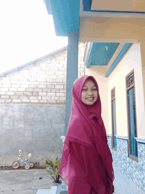 a woman in a pink hijab stands in front of a building