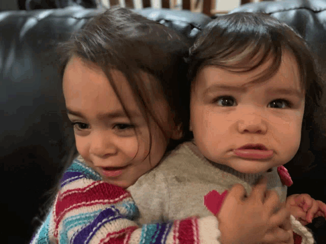 two little girls are sitting next to each other on a couch and one is wearing a sweater with a heart on it