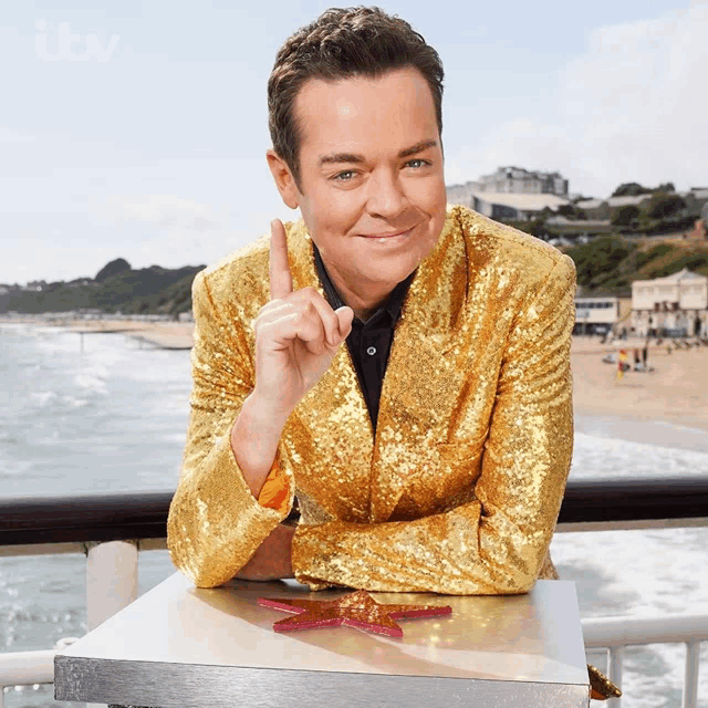 a man in a gold sequined jacket is sitting on a table with a starfish on it